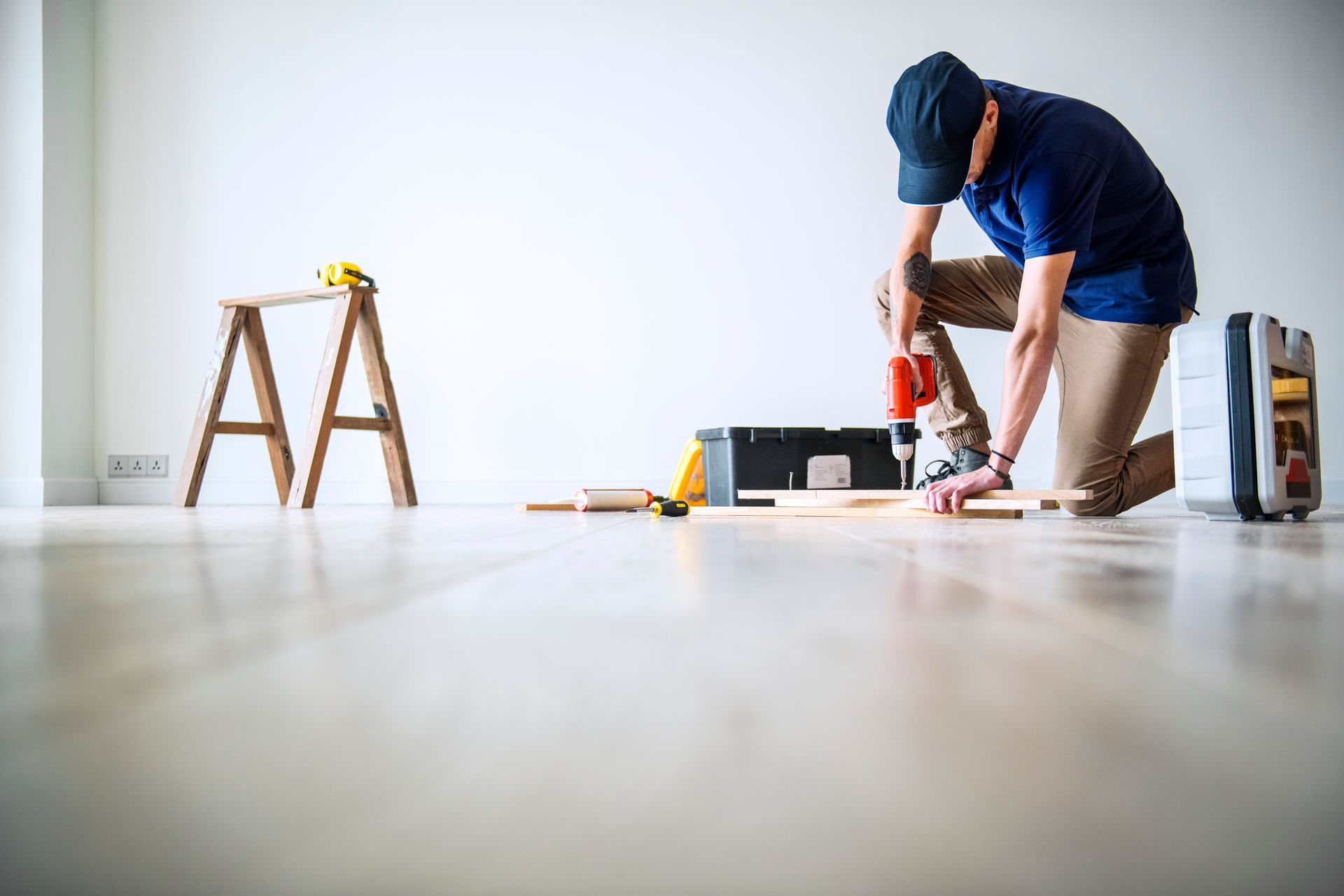 Man kneeling on the floor using a power drill during home renovation.