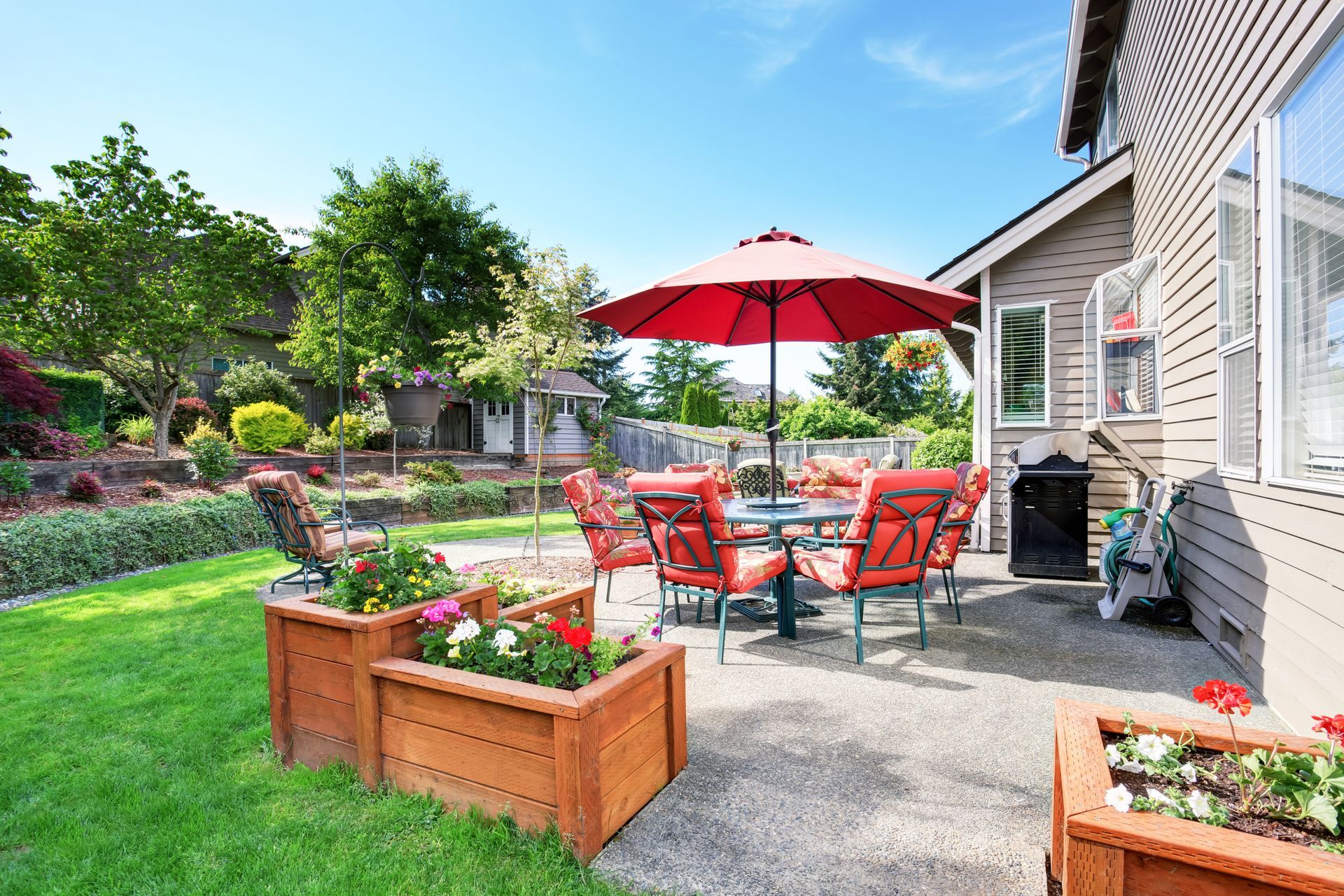 There is a patio with a table and chairs and a red umbrella.