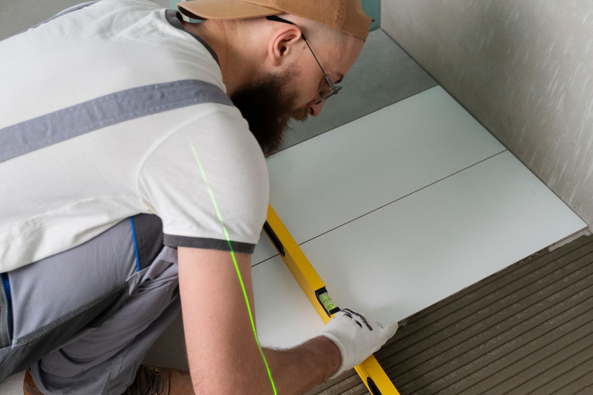 Worker installing floor tiles, using a level tool to ensure alignment during home renovation.