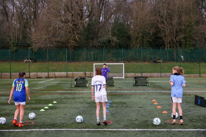 A group of young girls are standing on a soccer field with soccer balls.