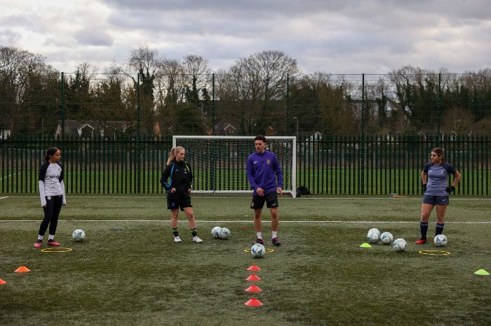 A group of people are standing on a soccer field with soccer balls.