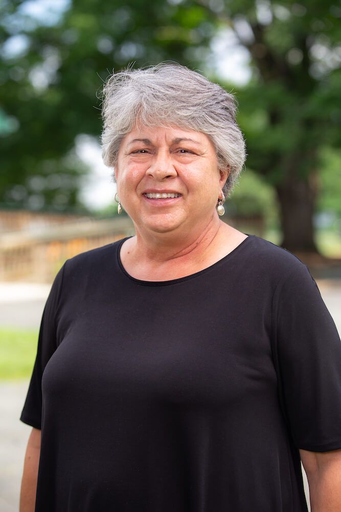 Woman with gray hair smiles at the camera, wearing a black top outdoors.