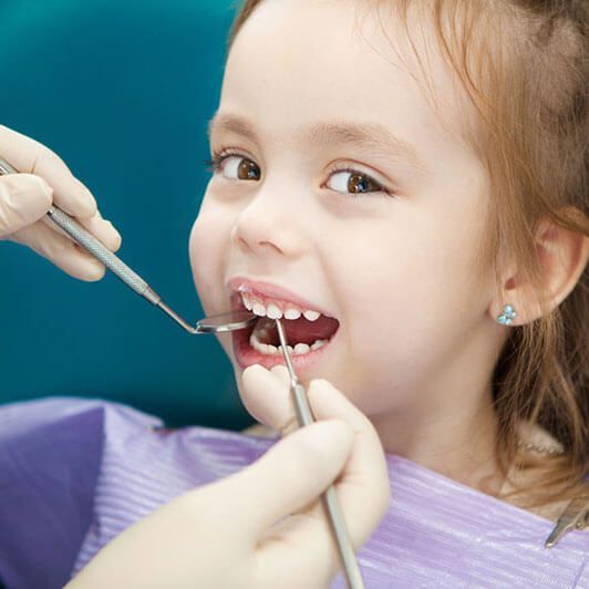a little girl is getting her teeth examined by a dentist .