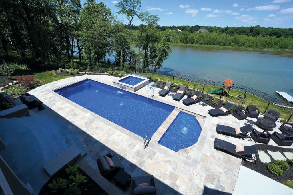 Rectangular swimming pool and hot tub overlooking a river. Lounge chairs and seating area.