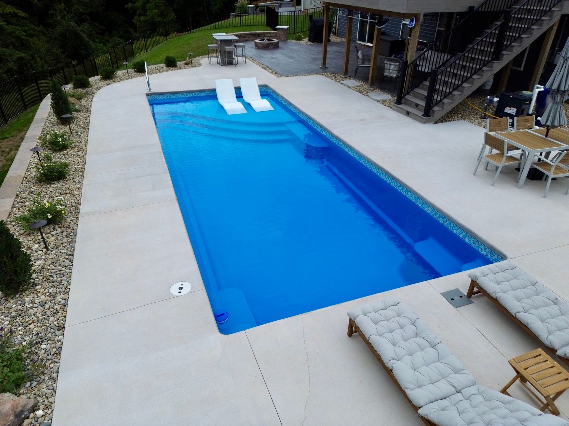 Rectangular swimming pool with white slides, surrounded by concrete patio and outdoor furniture.