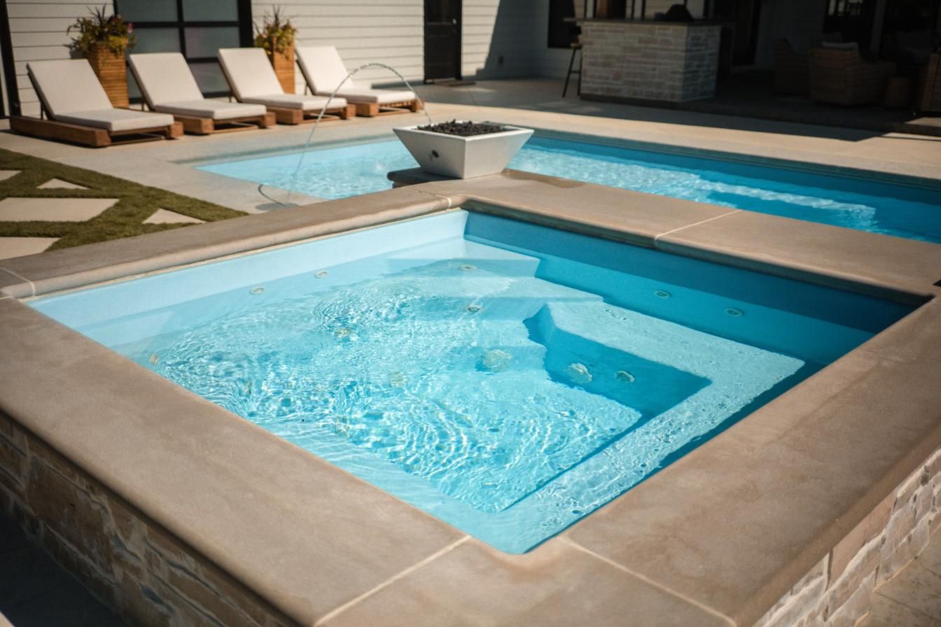 Outdoor pool area with multiple pools, lounge chairs, and a fire pit. Blue water, concrete surround.