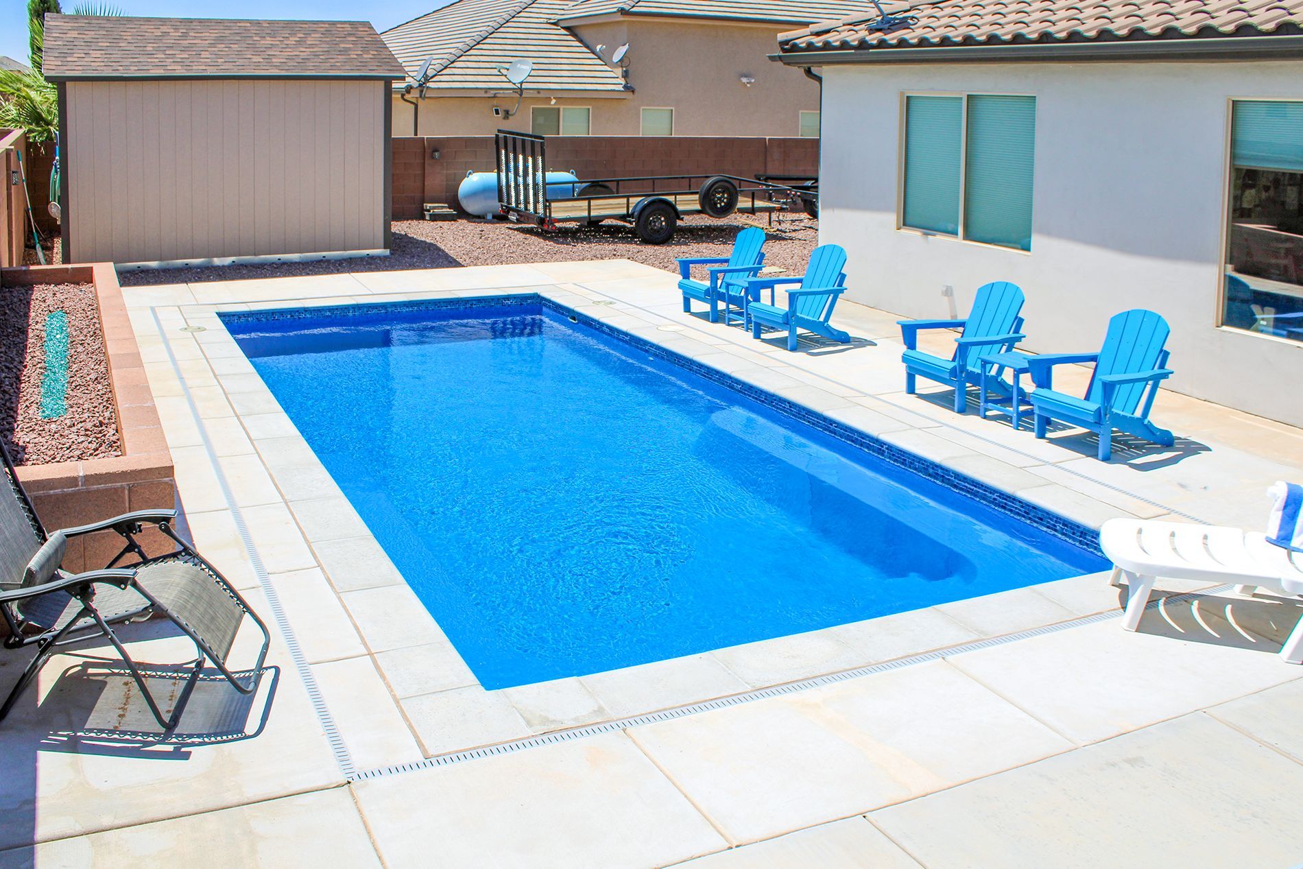 Rectangular swimming pool in a backyard with blue chairs and a shed.