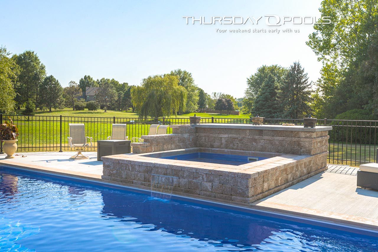 Outdoor swimming pool with jacuzzi, green lawn, trees, and blue sky.