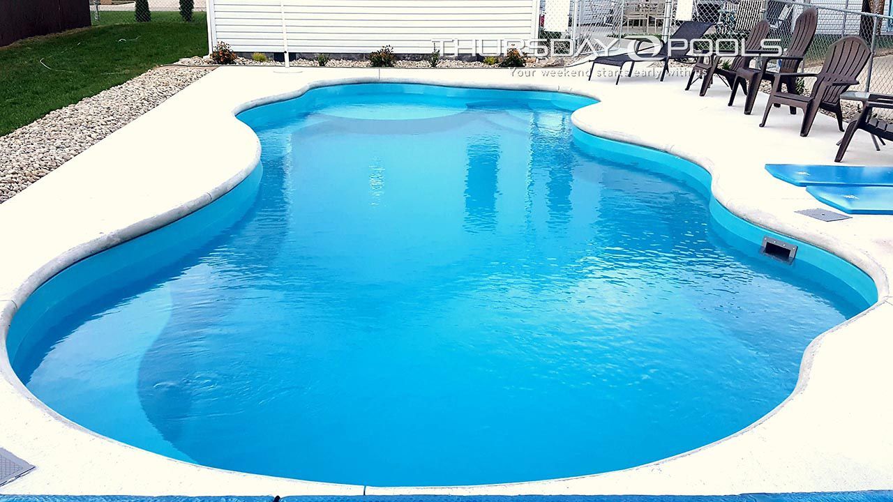A blue, kidney-shaped swimming pool with a white concrete deck in a sunny outdoor setting.