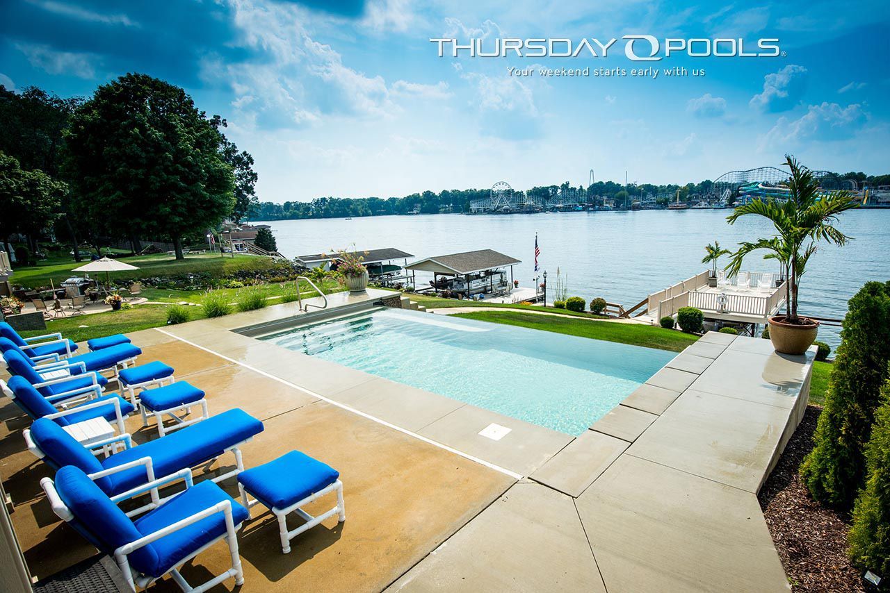 Poolside scene with blue lounge chairs, overlooking a lake with a cabana and trees.