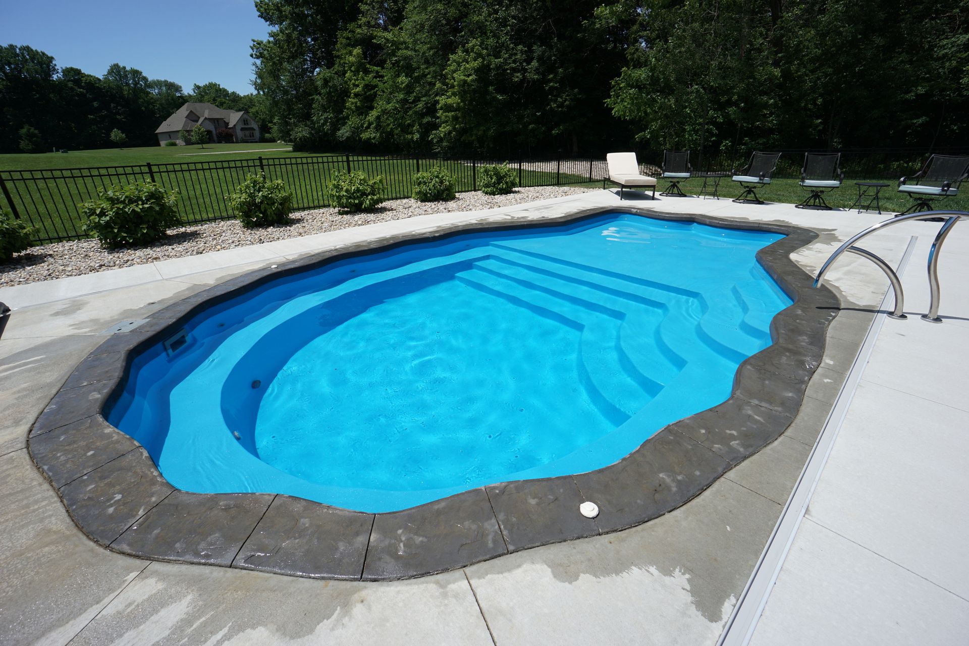 A bright blue swimming pool with steps, surrounded by gray stone and white concrete patio.