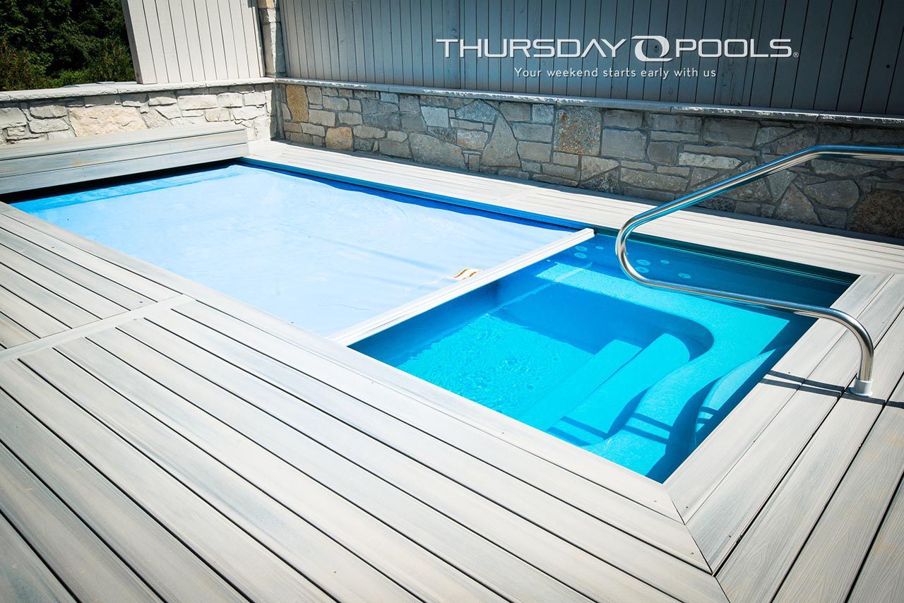 A small, rectangular in-ground swimming pool with steps, and a retractable cover on a wooden deck.