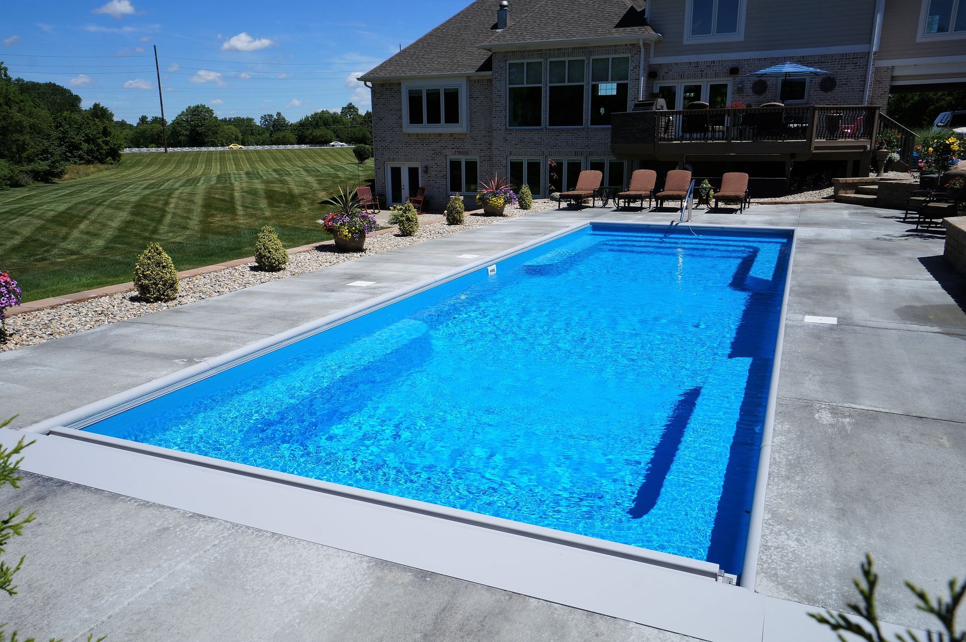 Rectangular blue swimming pool next to a house with a concrete patio.