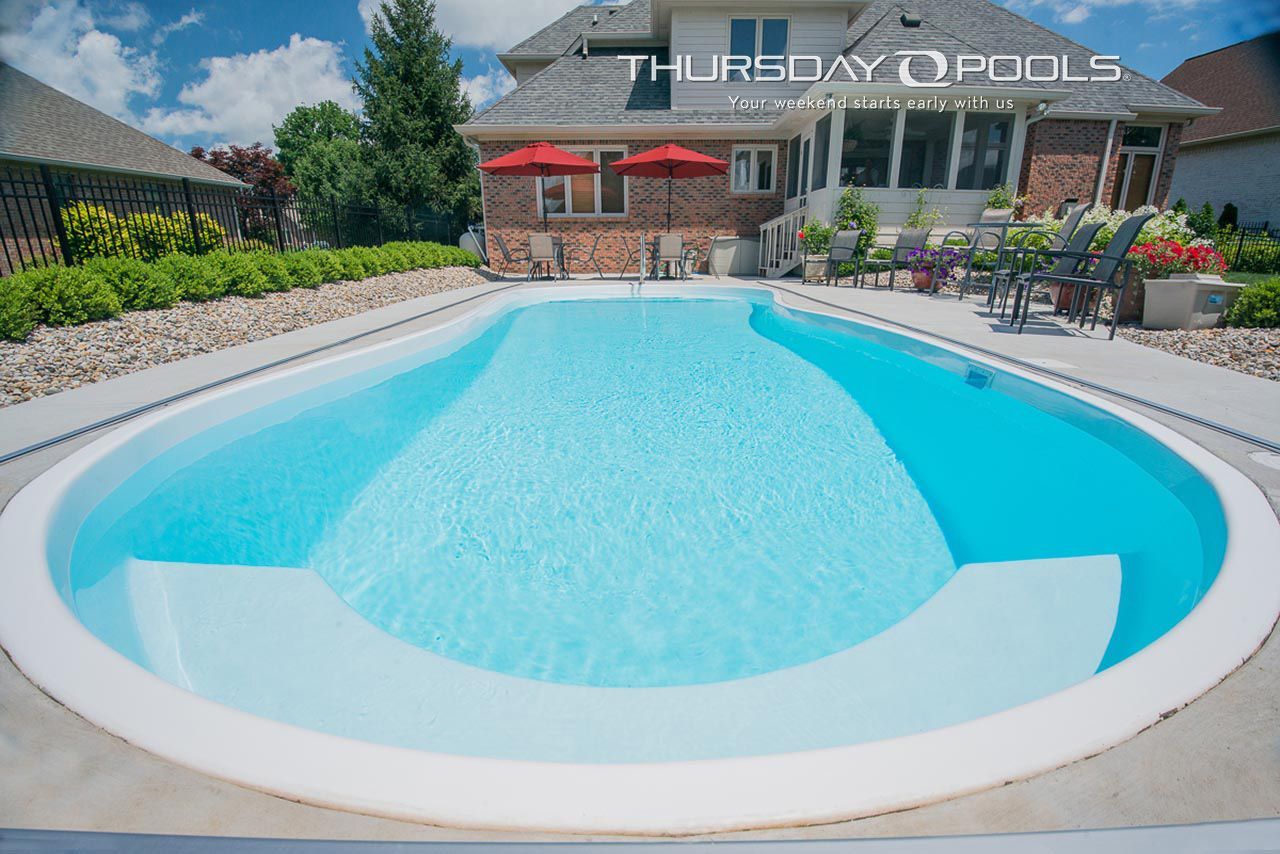 Oval-shaped swimming pool with blue water and white steps, set in a backyard near a house with red umbrellas.