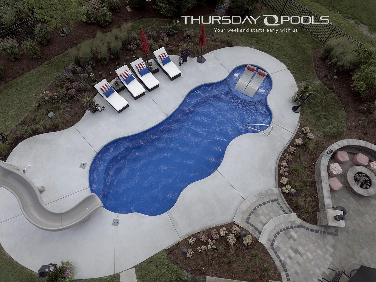 Aerial view of a custom blue pool with a slide, lounge chairs, and a paved patio.