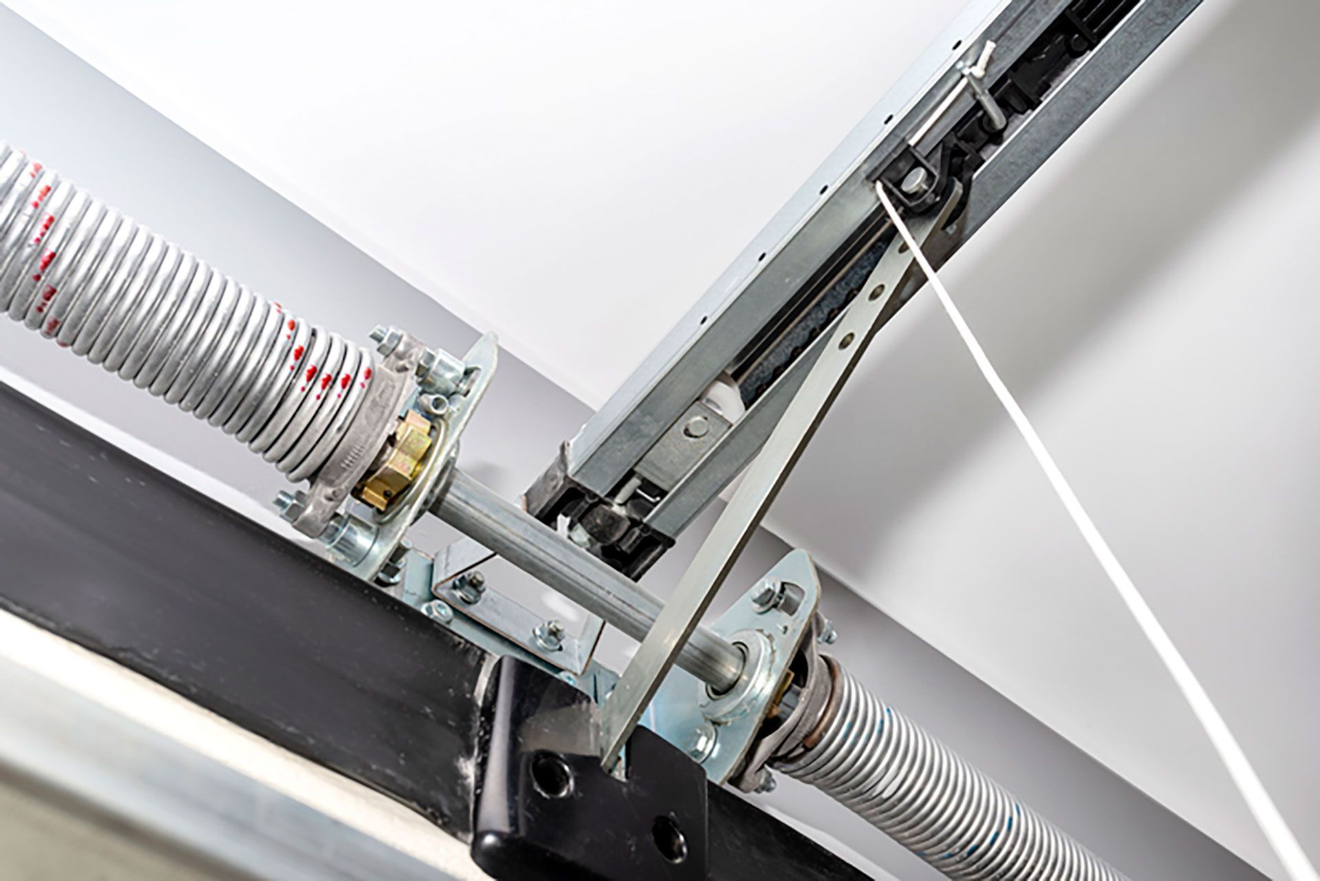 Close-up of a garage door spring and metal track mechanism against a white ceiling.