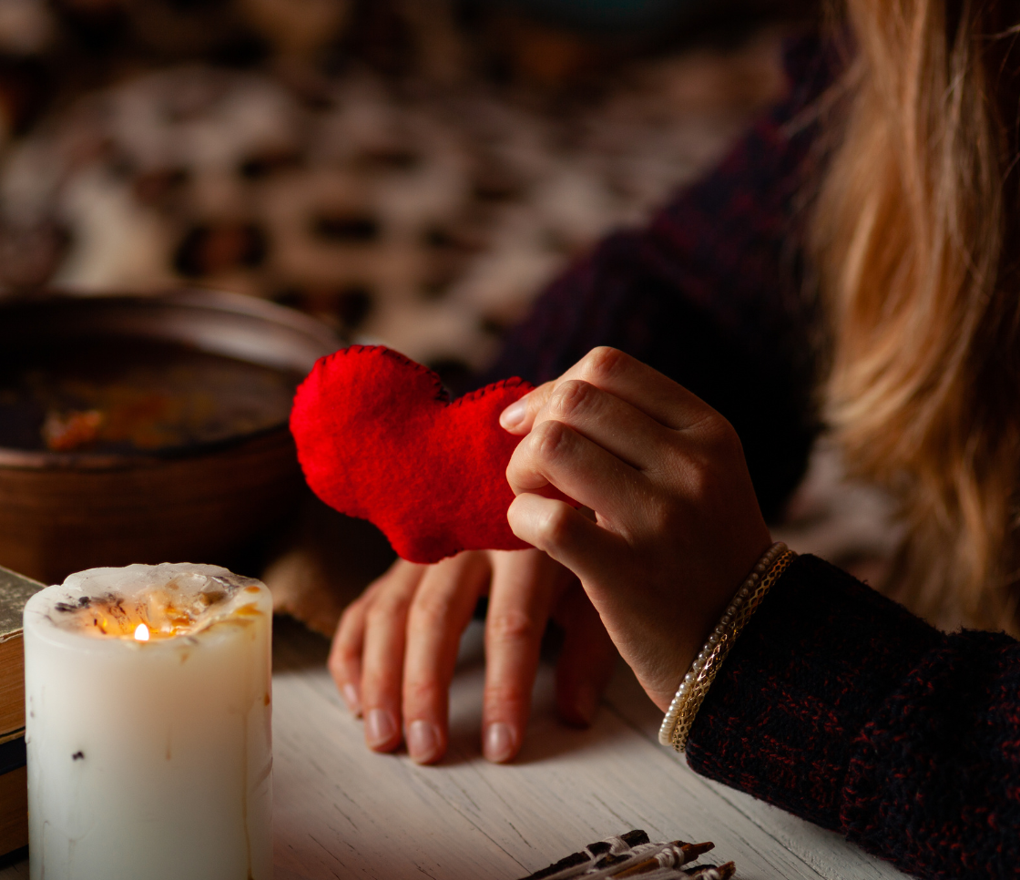 A woman is holding a red heart in her hands next to a candle.