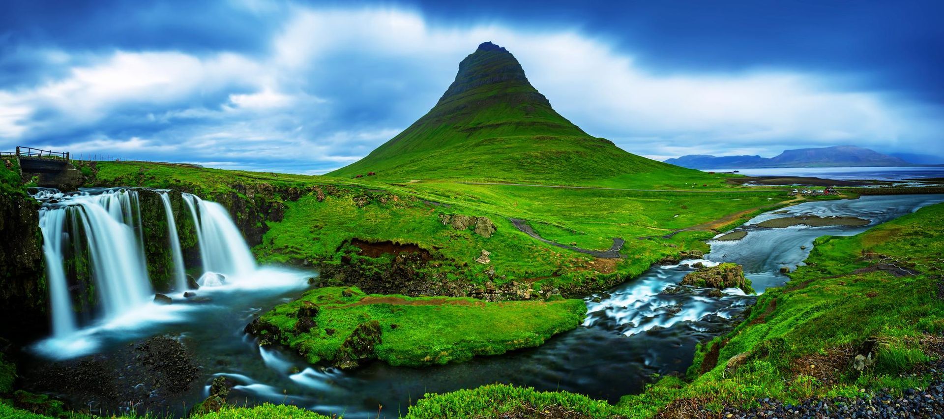 There is a waterfall in the foreground and a mountain in the background.