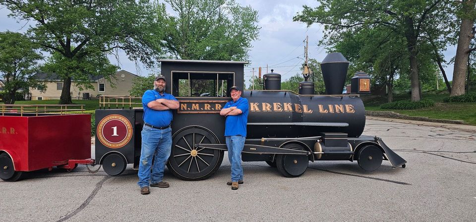Two men are standing in front of a train that says krackel line