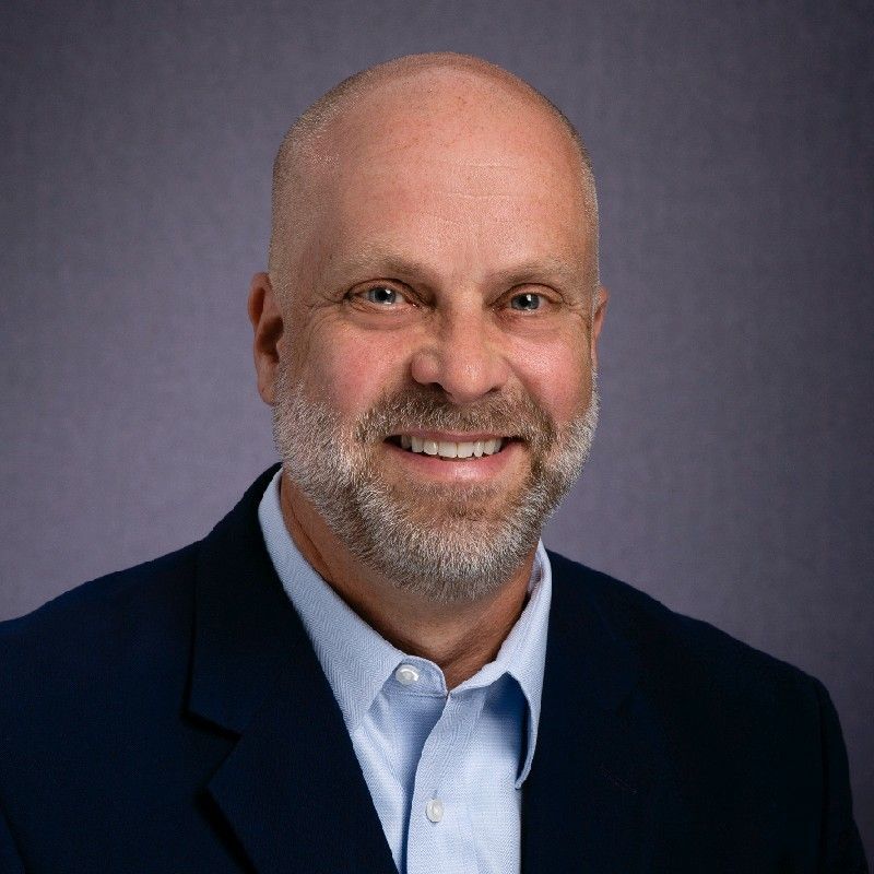 A bald man with glasses and a beard smiles for the camera