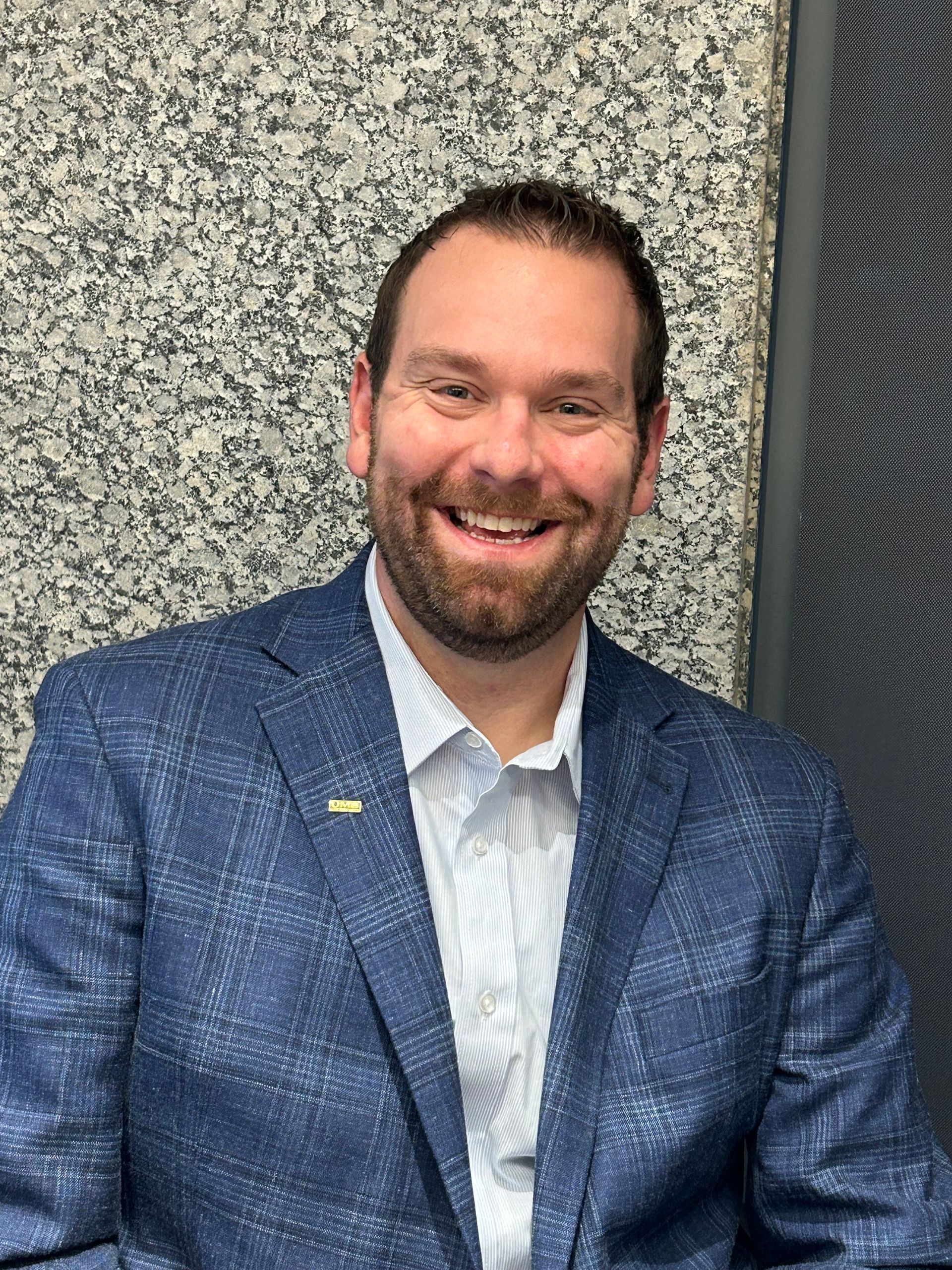 A man with glasses and a beard is wearing a hawaiian shirt and smiling.