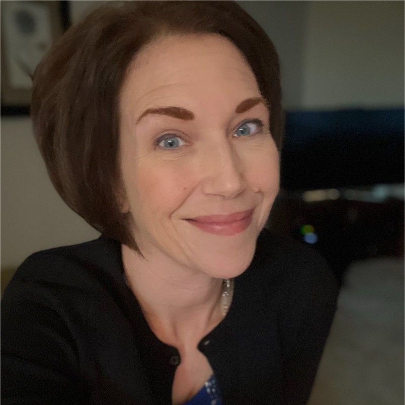A woman in a blue shirt is smiling and looking at the camera.
