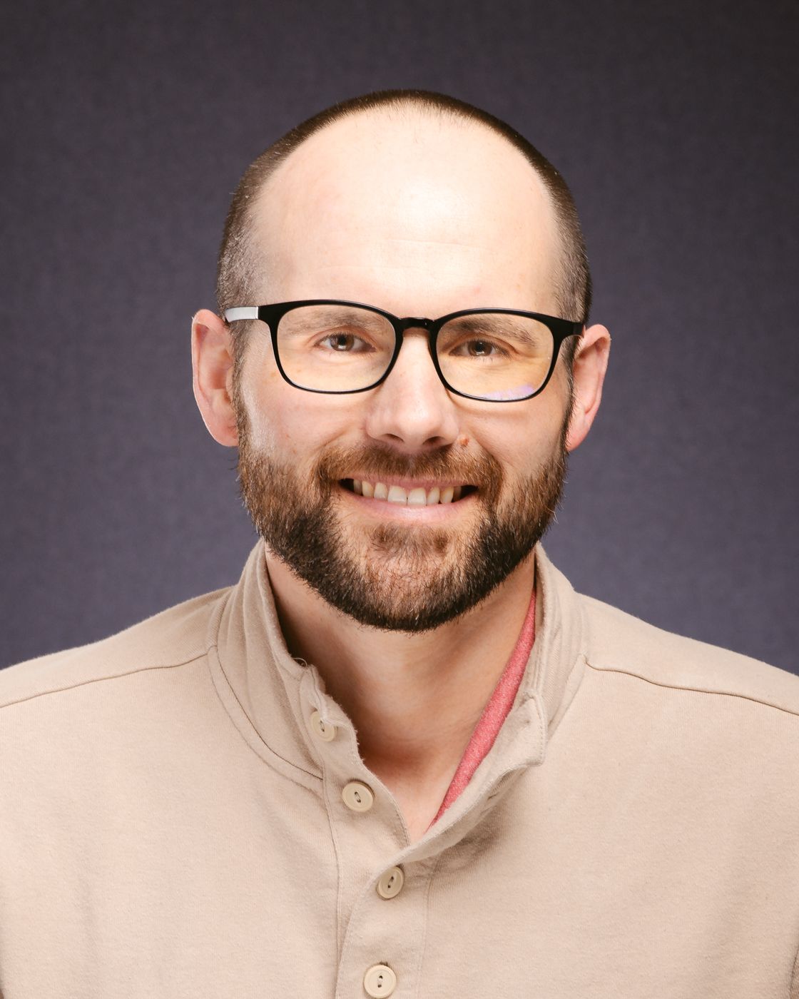 A bald man in a suit and blue shirt is smiling for the camera.
