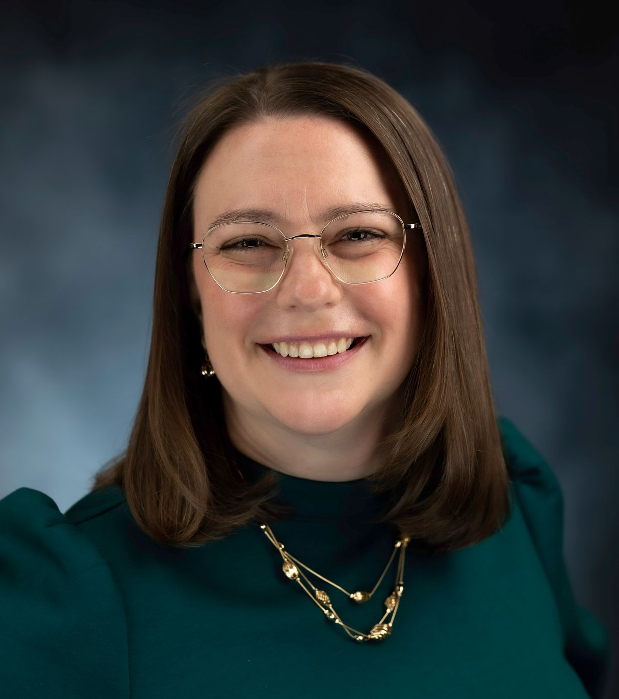 A woman wearing glasses and a necklace is smiling for the camera.