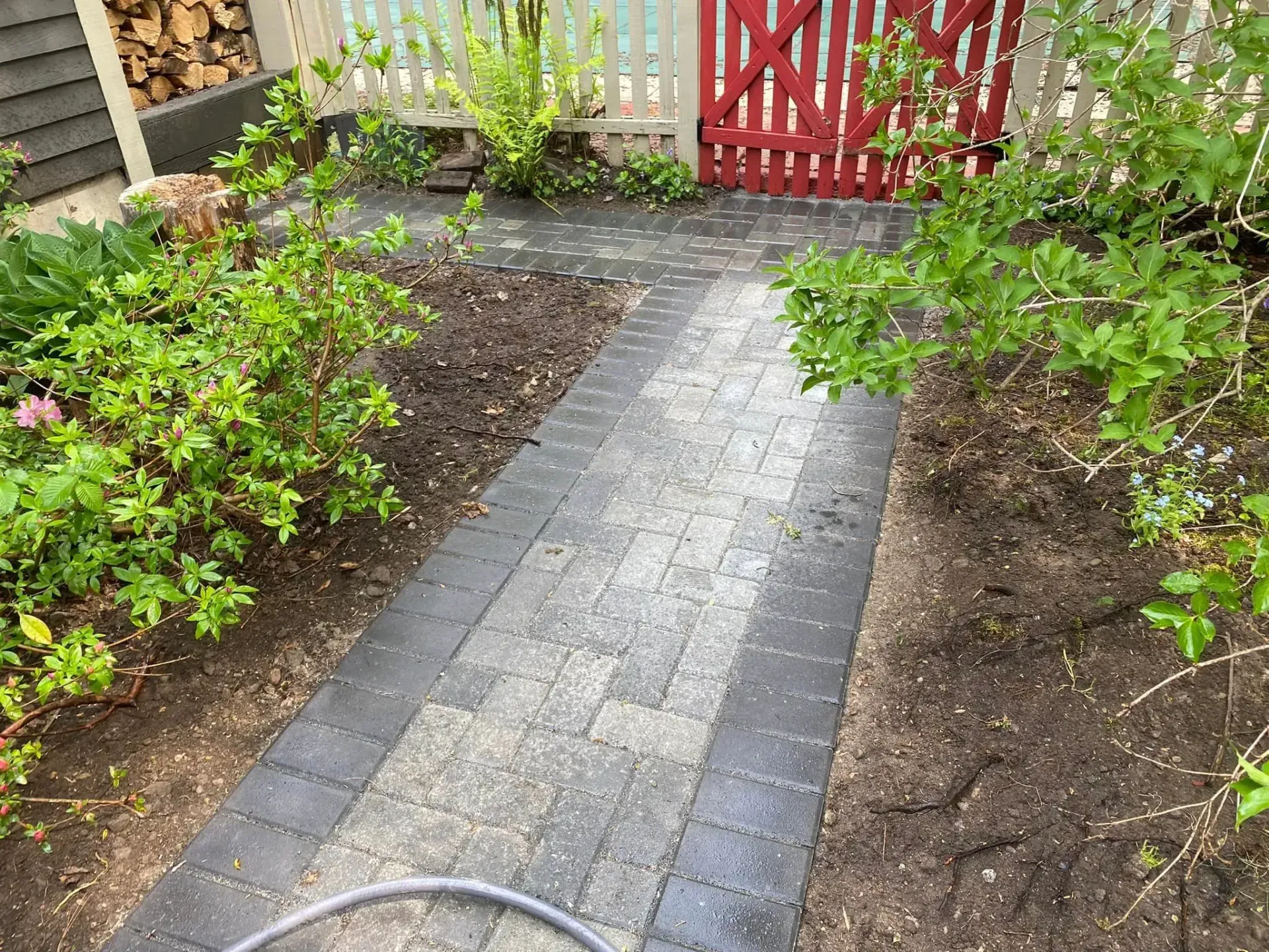 A brick walkway leading to a red gate in a garden.