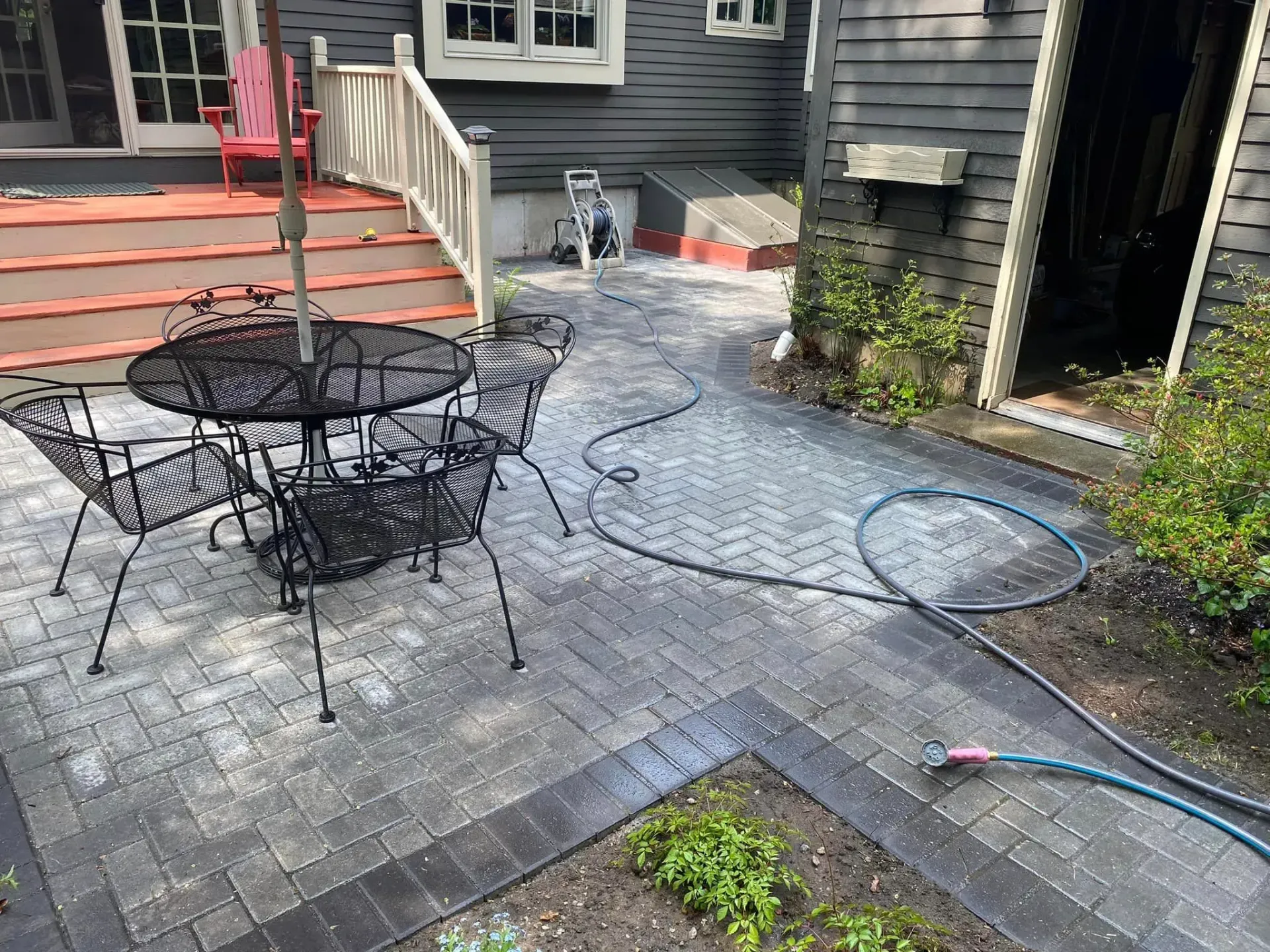 A patio with a table and chairs is being cleaned with a hose.