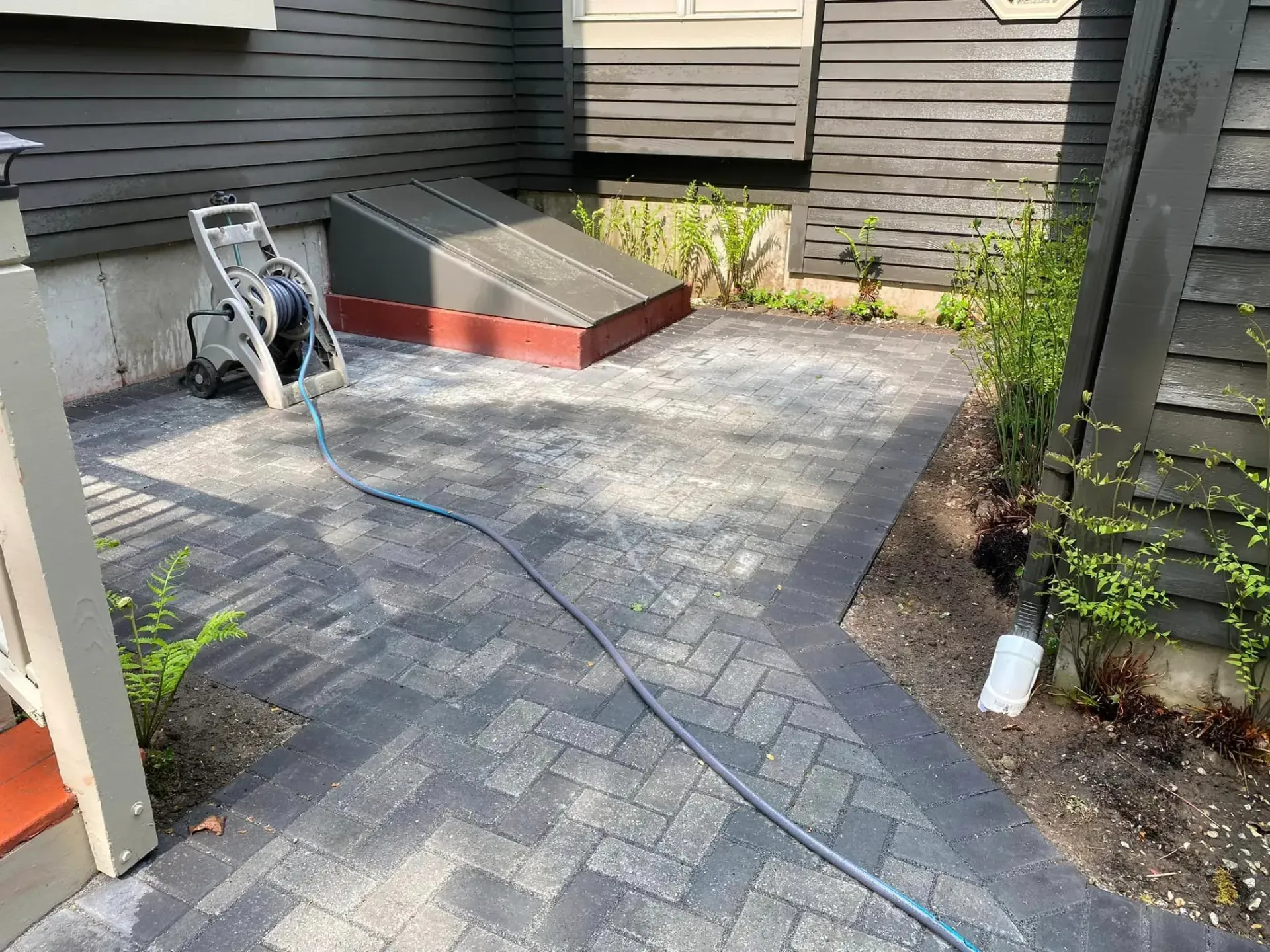 A hose is connected to a brick patio in front of a house.