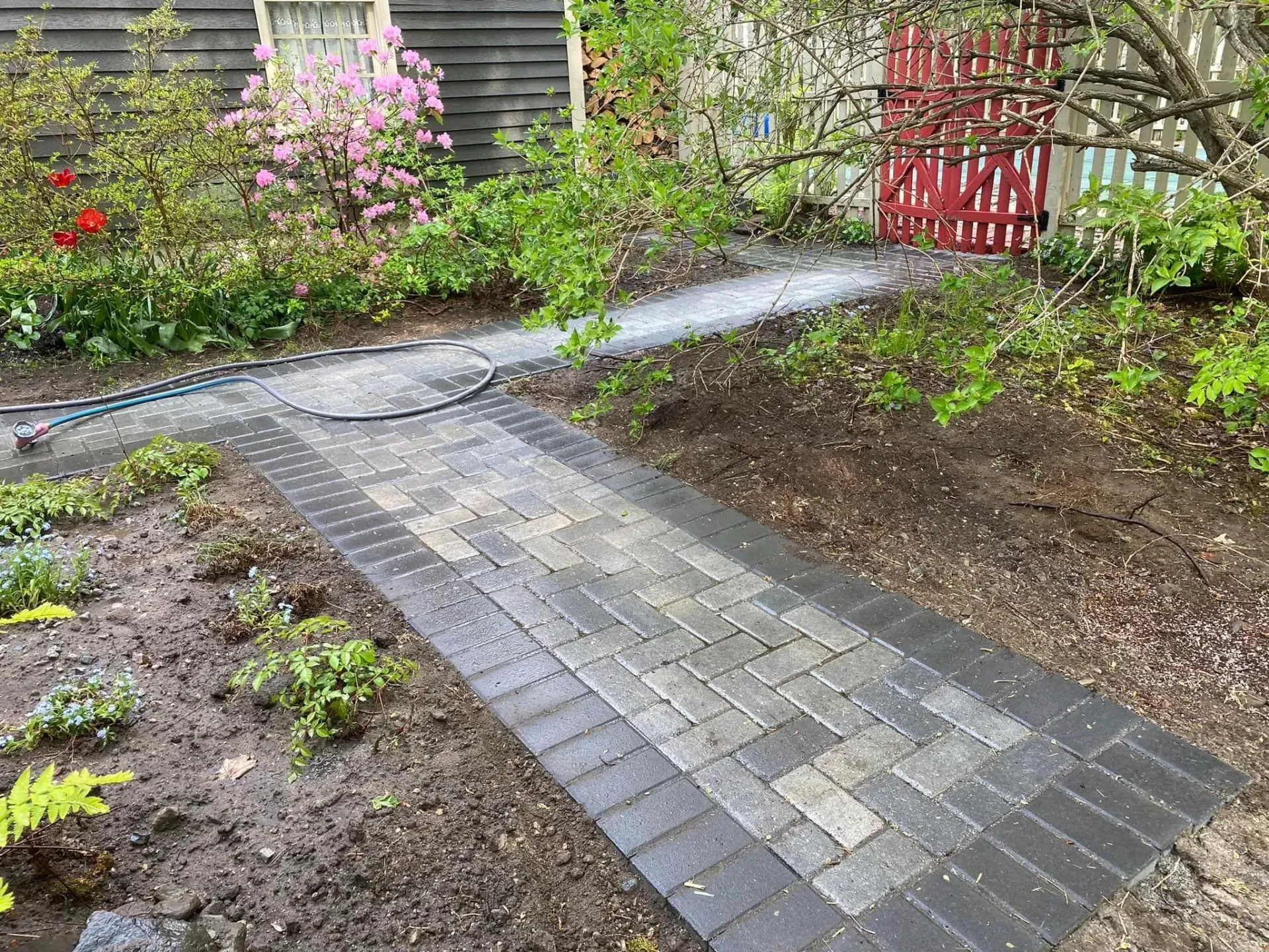 A brick walkway in a garden surrounded by trees and bushes.