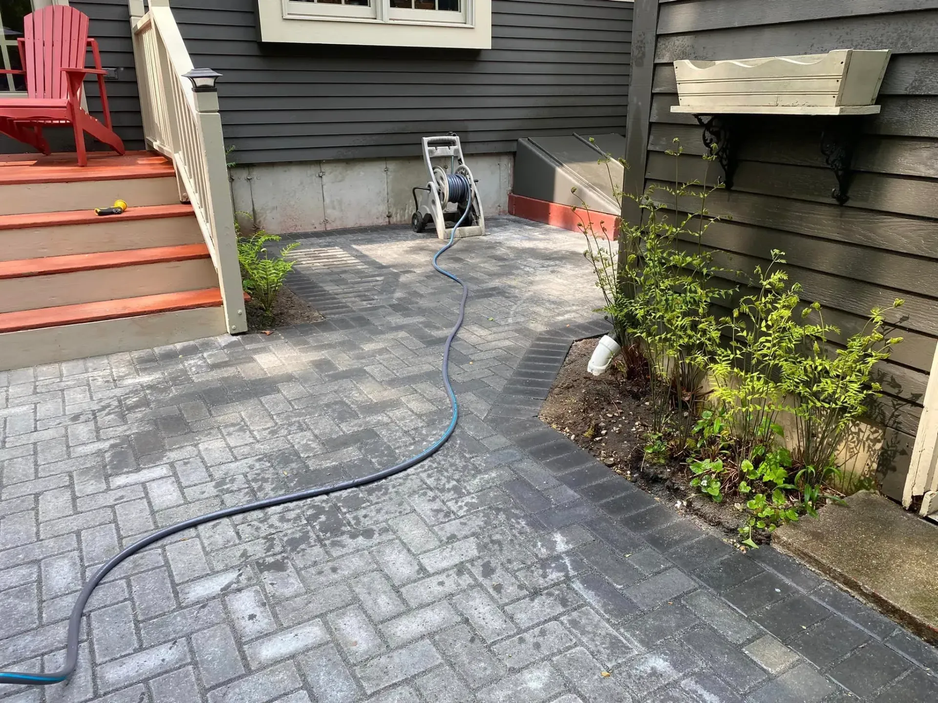 A hose is connected to a brick walkway in front of a house.