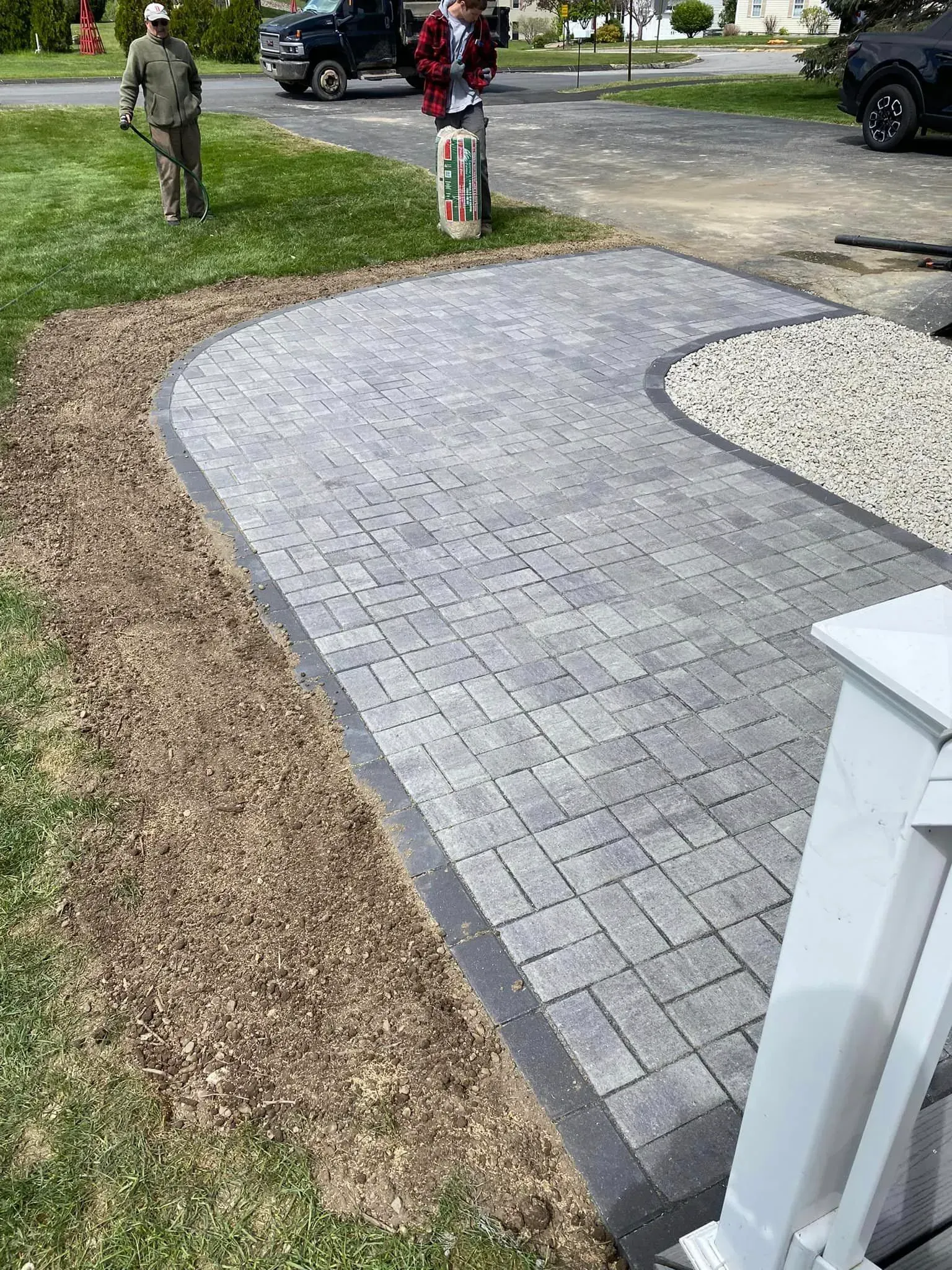 A man is standing next to a brick walkway in a driveway.