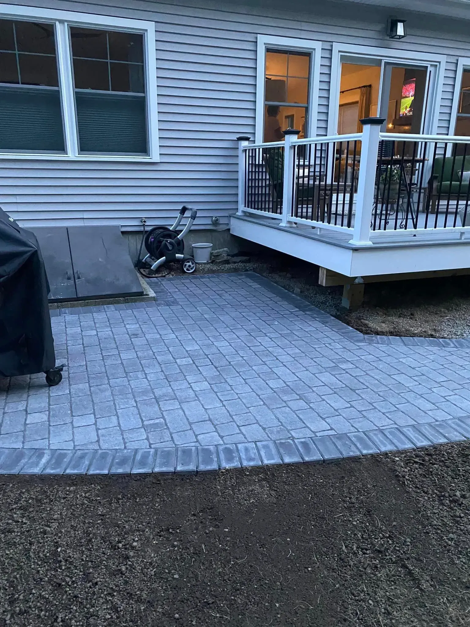 A patio with a deck and a grill in front of a house.