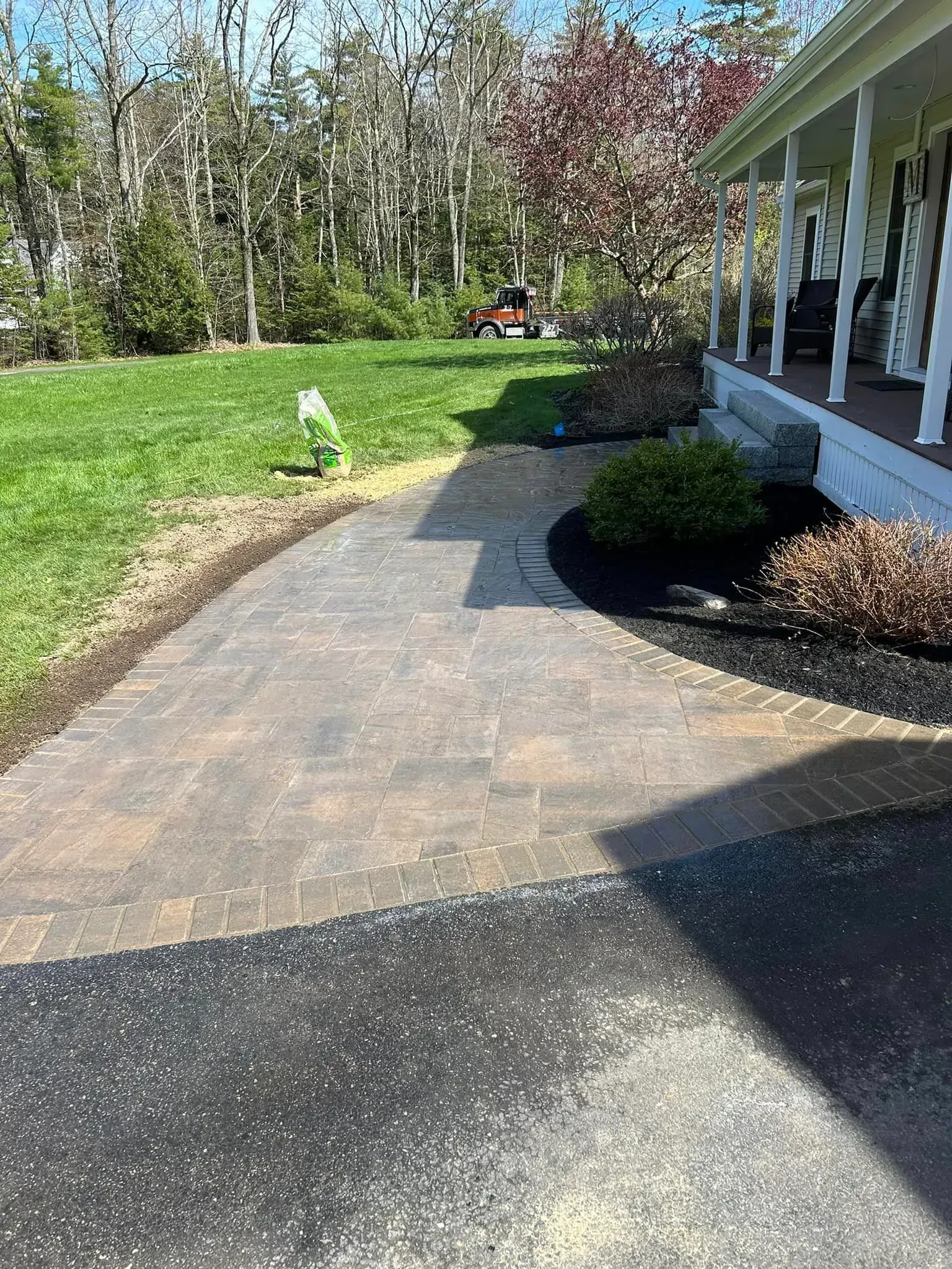 A brick walkway leading to a house with a broom in the grass.