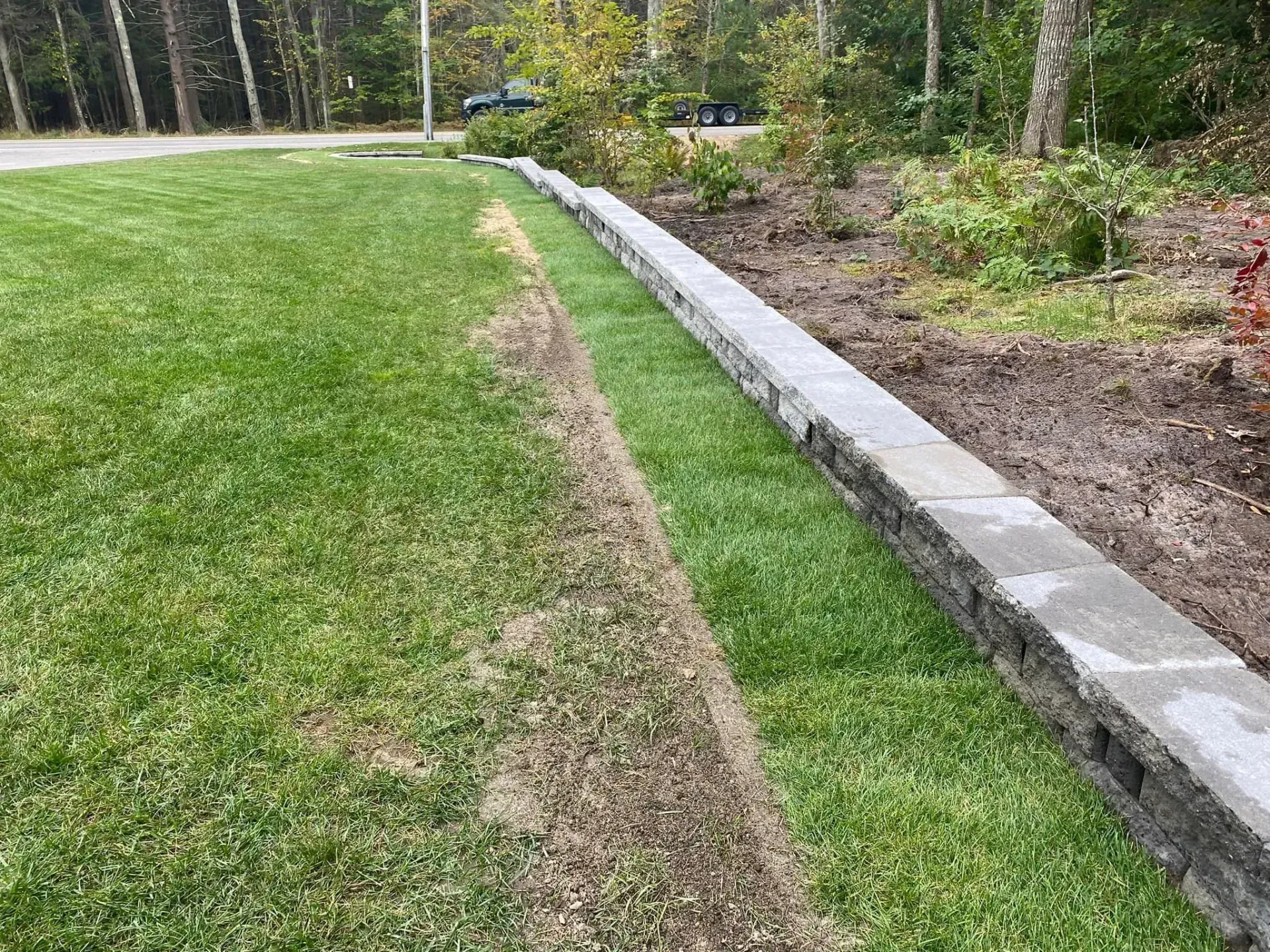 A lush green lawn with a stone wall along the side of it.