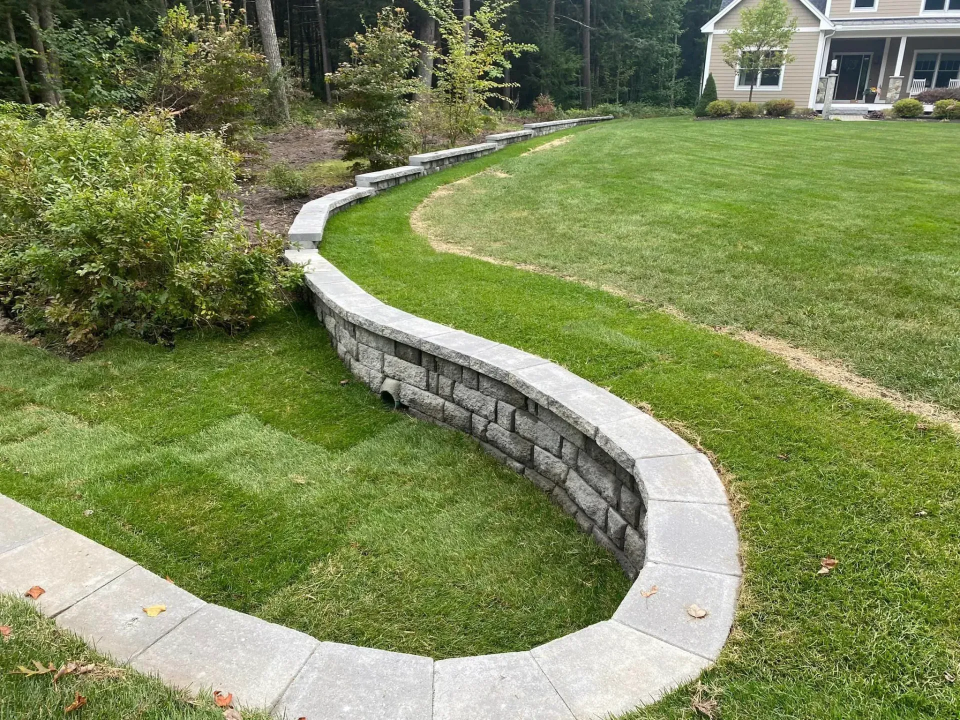 A curved stone wall surrounds a lush green lawn in front of a house.