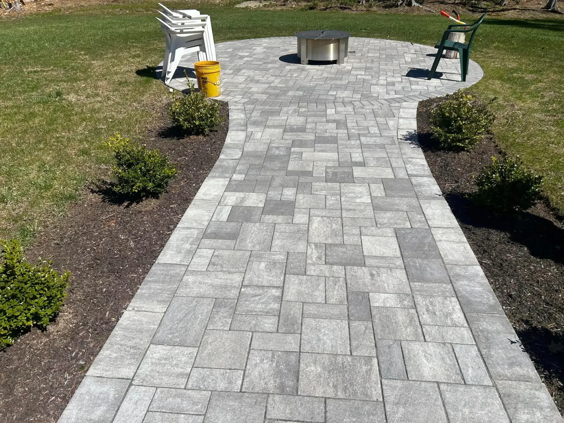 A brick walkway leading to a fire pit in a backyard.