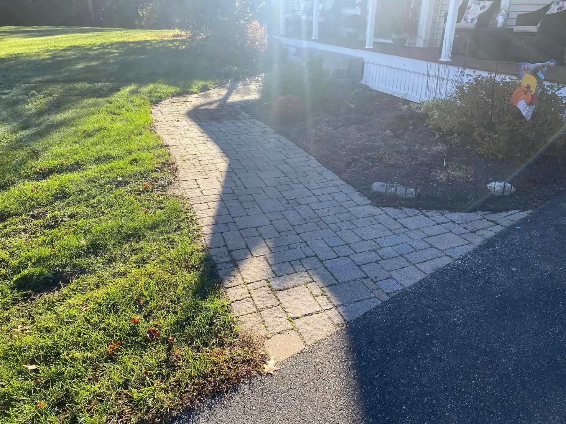 A brick walkway leading to a house with a broom in the grass.