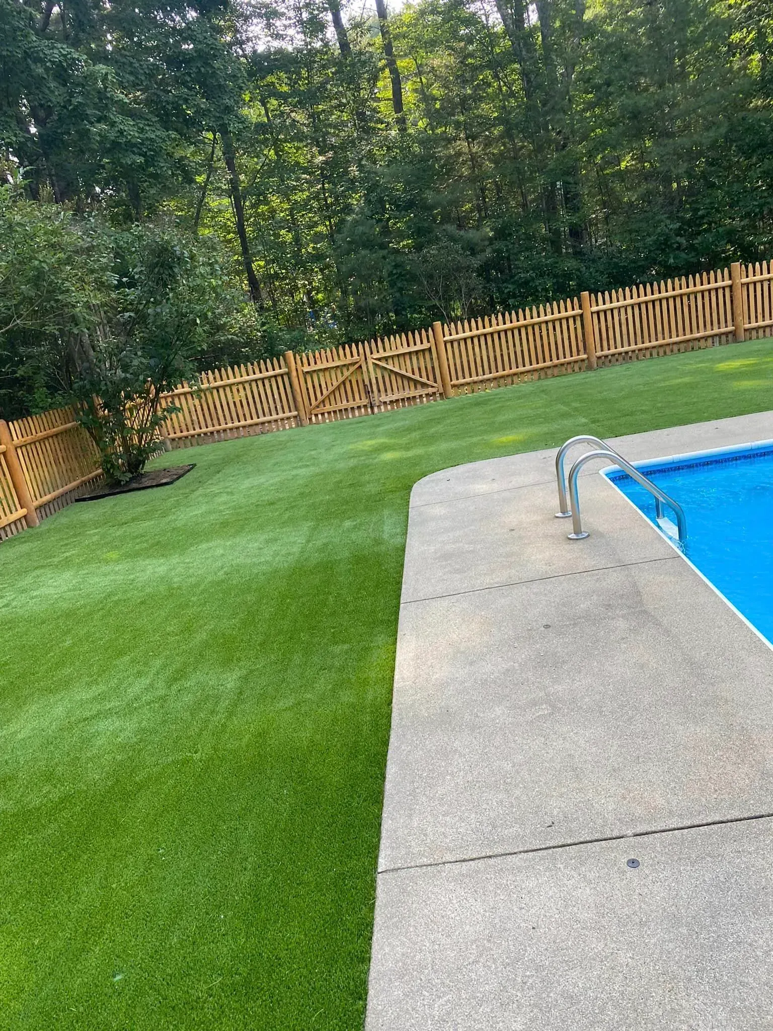 A swimming pool surrounded by a lush green lawn and a wooden fence.