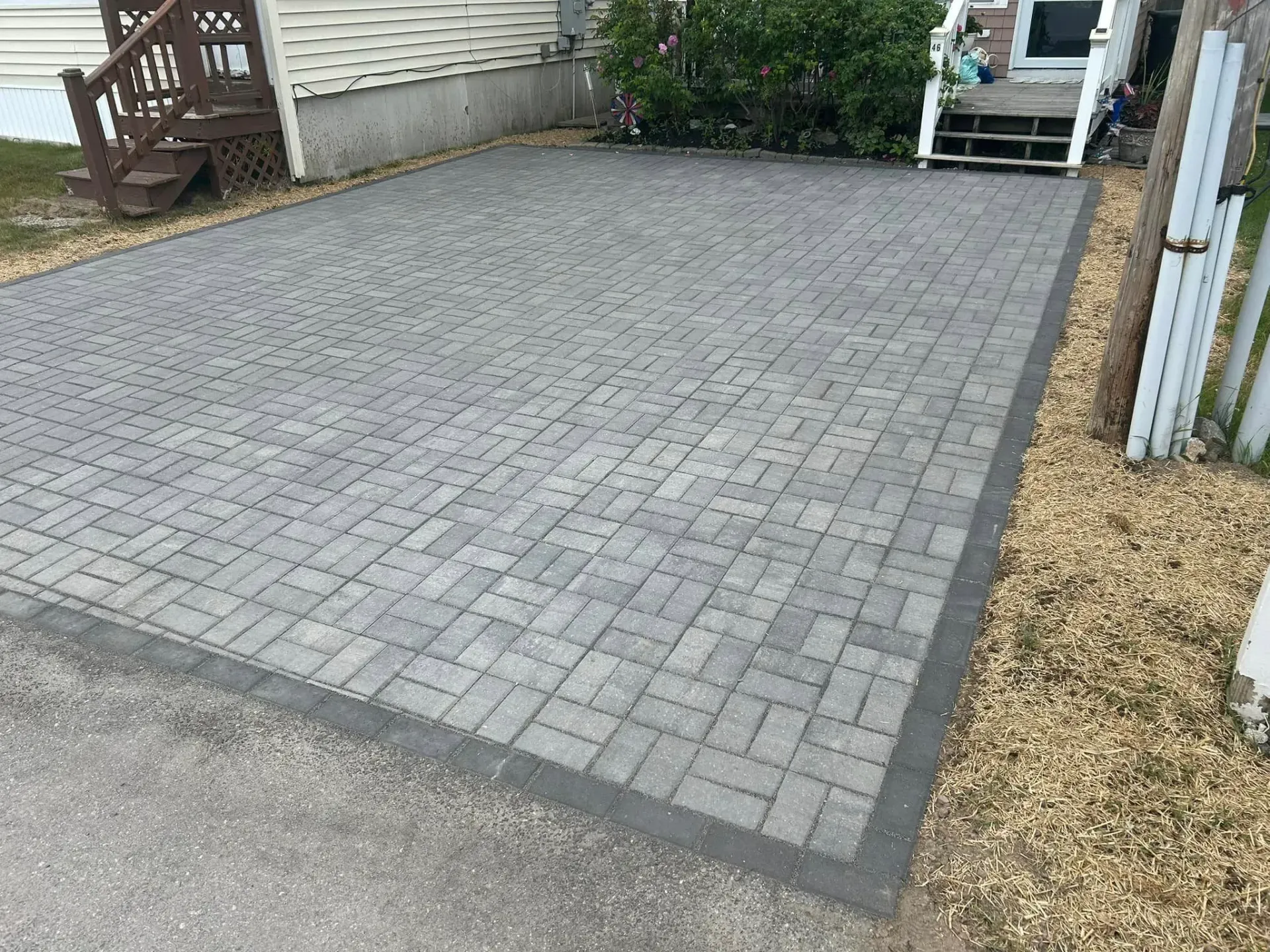 A brick driveway in front of a house with a white fence.