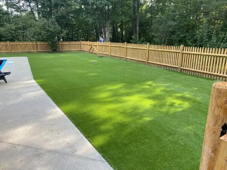 A backyard with a wooden fence and artificial grass.