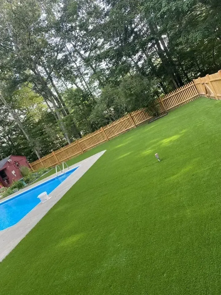 A swimming pool surrounded by a lush green lawn and a wooden fence.