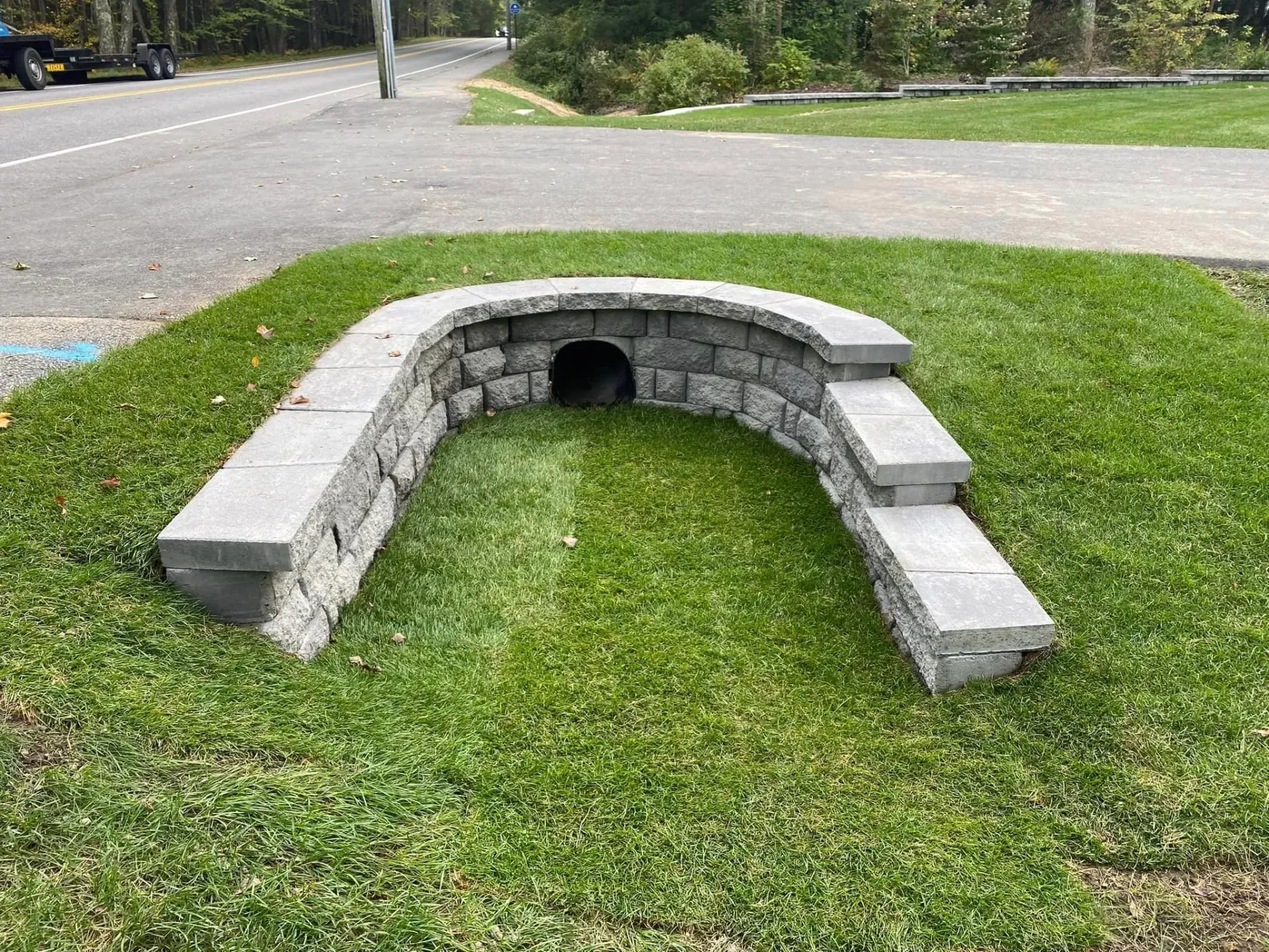A stone wall with a hole in the middle of it in the grass.