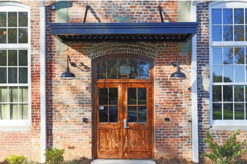 Exterior entrance with wooden double doors and brick wall.