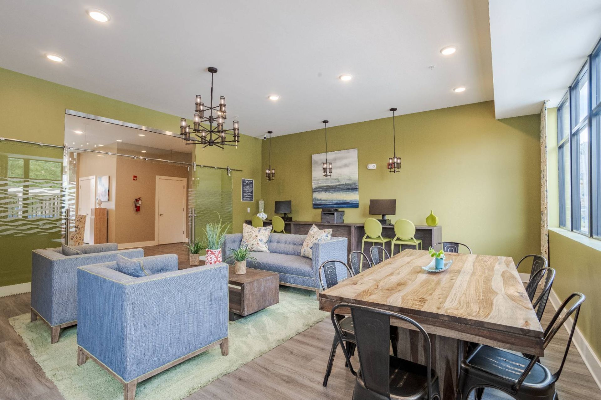 Interior of a community lounge with blue seating, a large wooden table, and green walls.