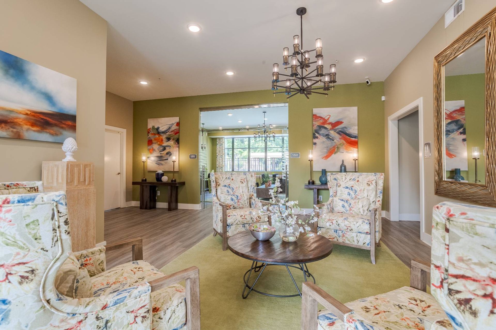 Lobby seating area with floral upholstered chairs, a round coffee table, and abstract art on green walls.