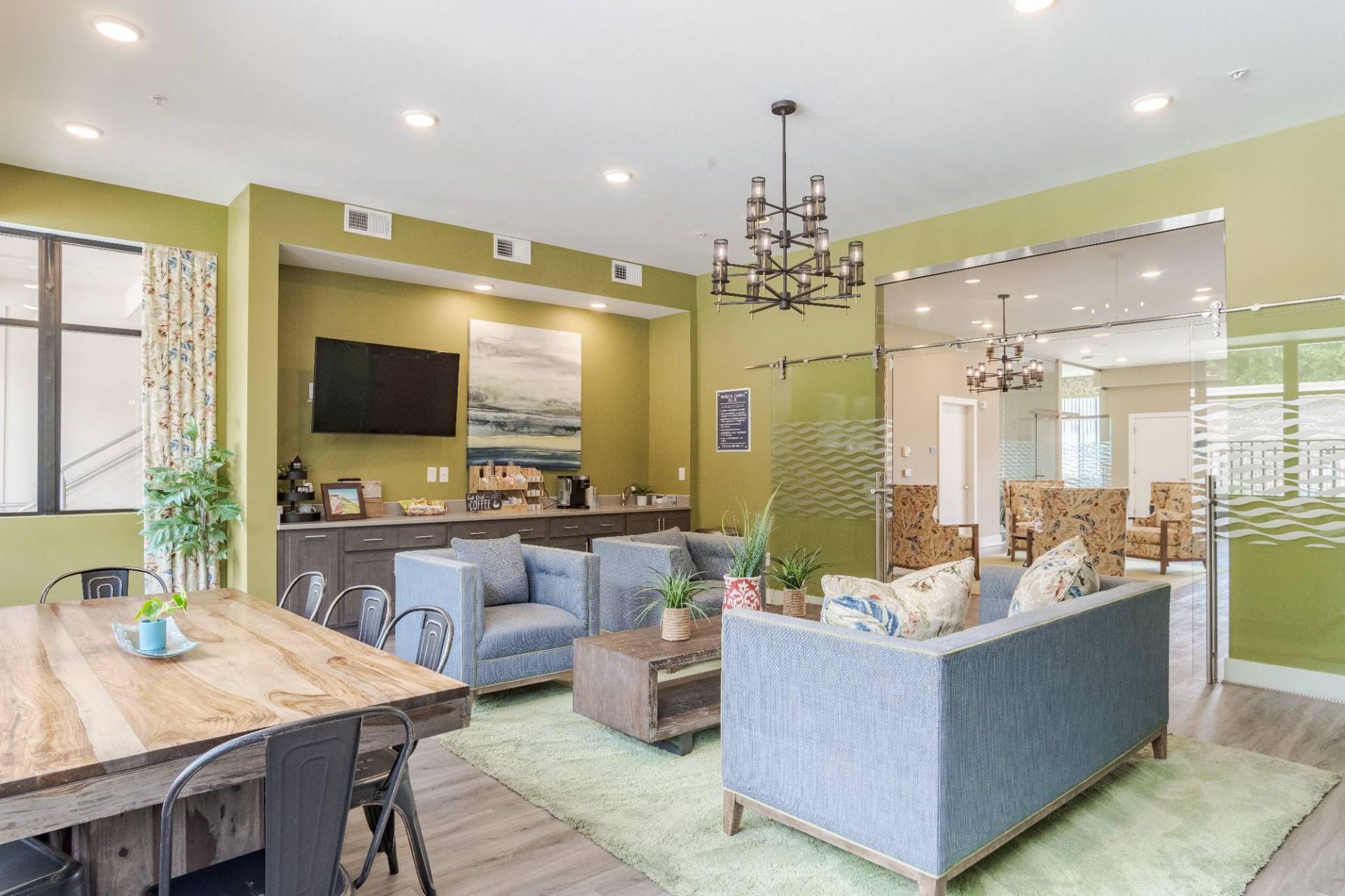 Interior of a modern apartment community lounge with blue couches, a coffee bar, and a glass-walled area.