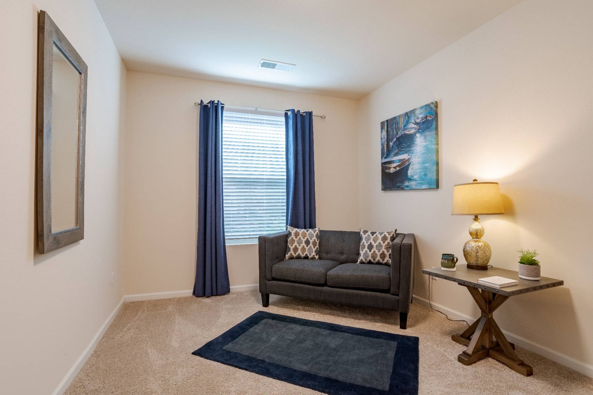Cozy living room with gray sofa, blue curtains, wall art, and a side table lamp.